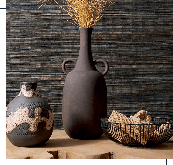 A vase and bowl on a table with a wall behind it.